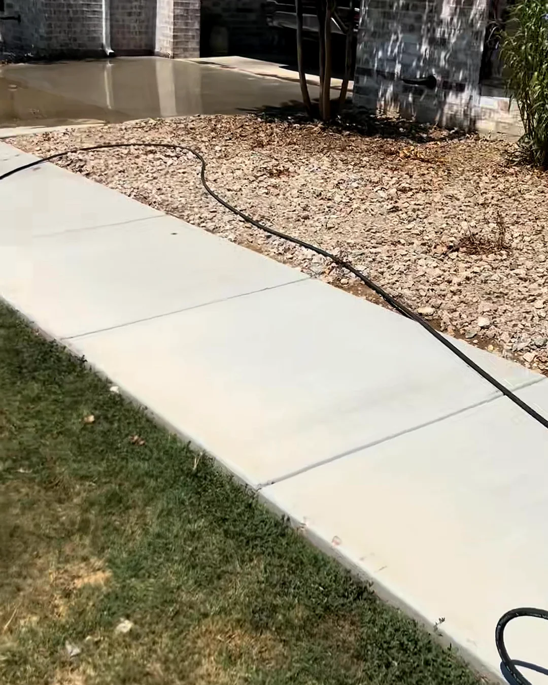 A clean concrete sidewalk running along a lawn toward a brick house