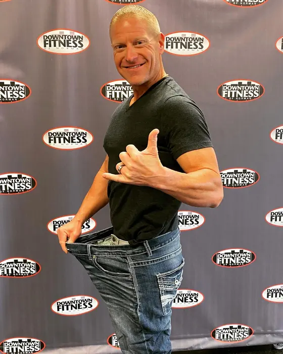 Mark Floyd, owner of Downtown Fitness, wearing the size 44 jeans from 2017 and pulling the waistband out to show the gap
