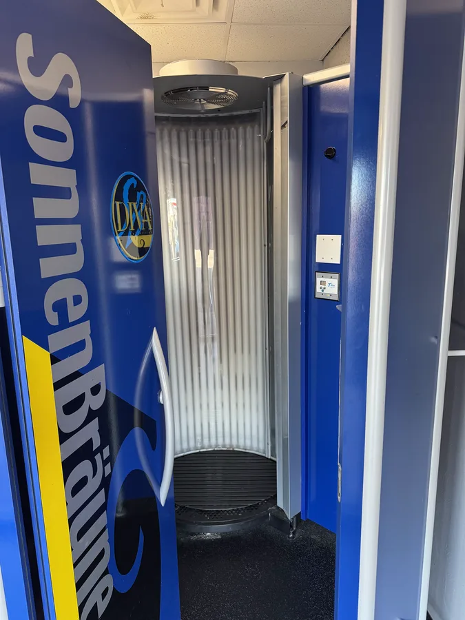 Inside a stand-up tanning booth, the door open on the ring of lamps