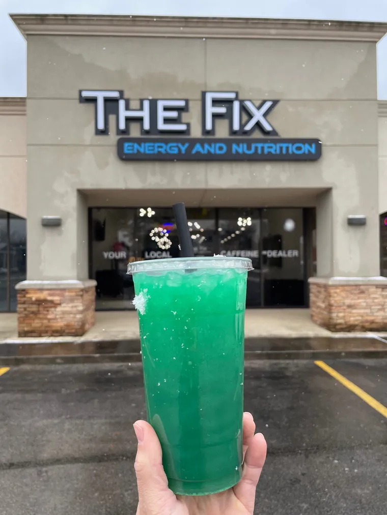 A green tea held up outside the storefront under THE FIX sign